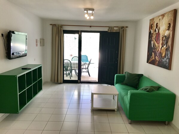 A living room with a green sofa, a white coffee table, a green cabinet, a television on the wall, and a painting.