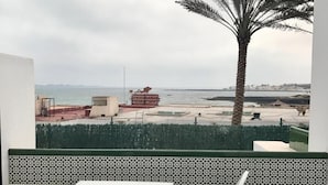 A balcony with a view of the sea, a palm tree, and a patterned wall.