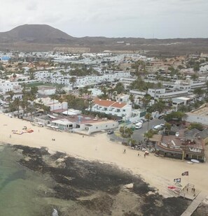 A coastal town with white buildings, a sandy beach, and a mountain in the background.