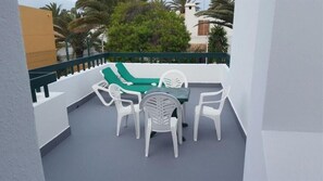 Een balkon met witte plastic stoelen en een tafel, omgeven door een witte balustrade.