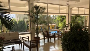 Un espacio interior amplio con un gran ventanal, un sofá, sillas de madera, una mesa y varias plantas en macetas.
