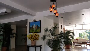 Un vestíbulo amplio con una televisión grande, plantas en macetas y un área de comedor con vistas a zonas verdes.