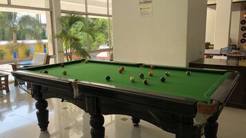 Une table de billard dans un espace intérieur bien éclairé, avec un panneau « Il est interdit de fumer » accroché au mur.