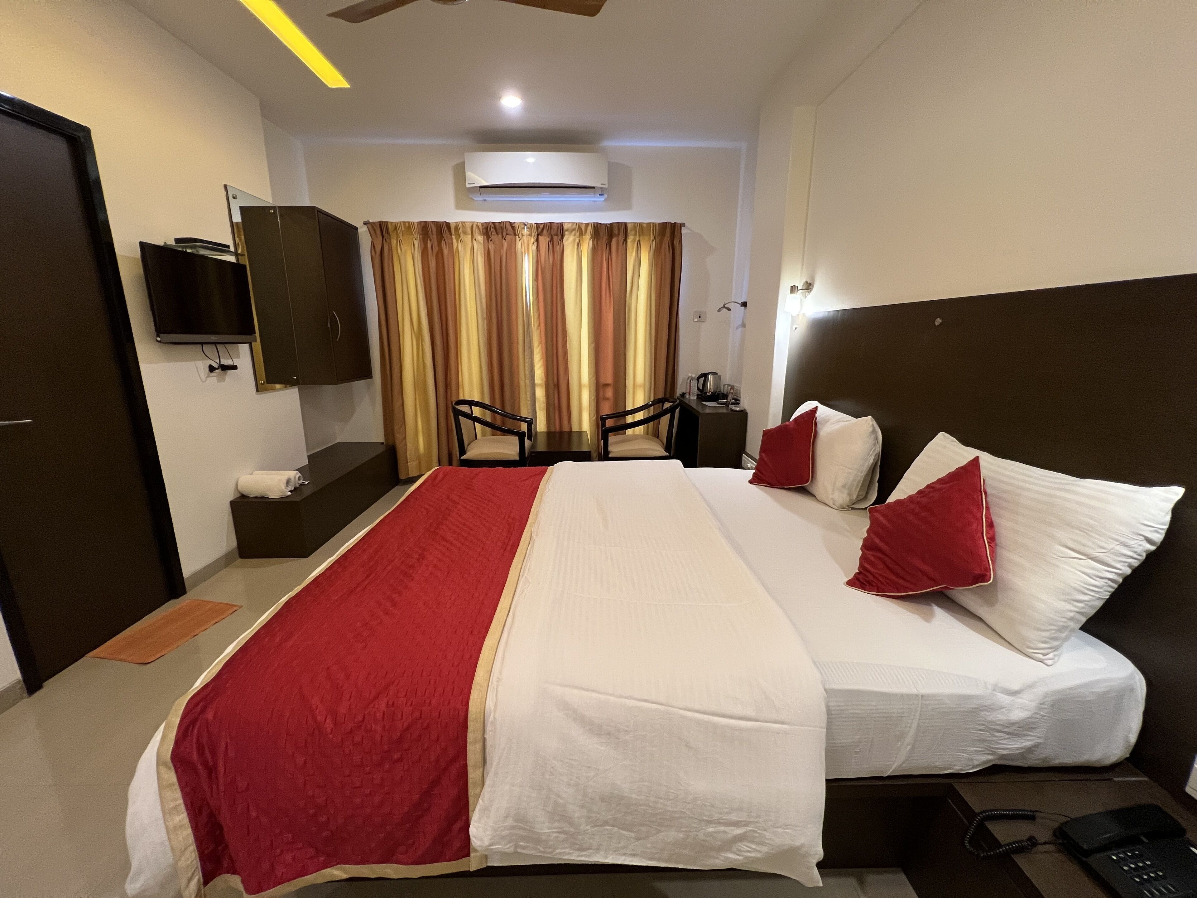 A hotel room with a bed, a desk, a chair, a television, and an air conditioning unit.