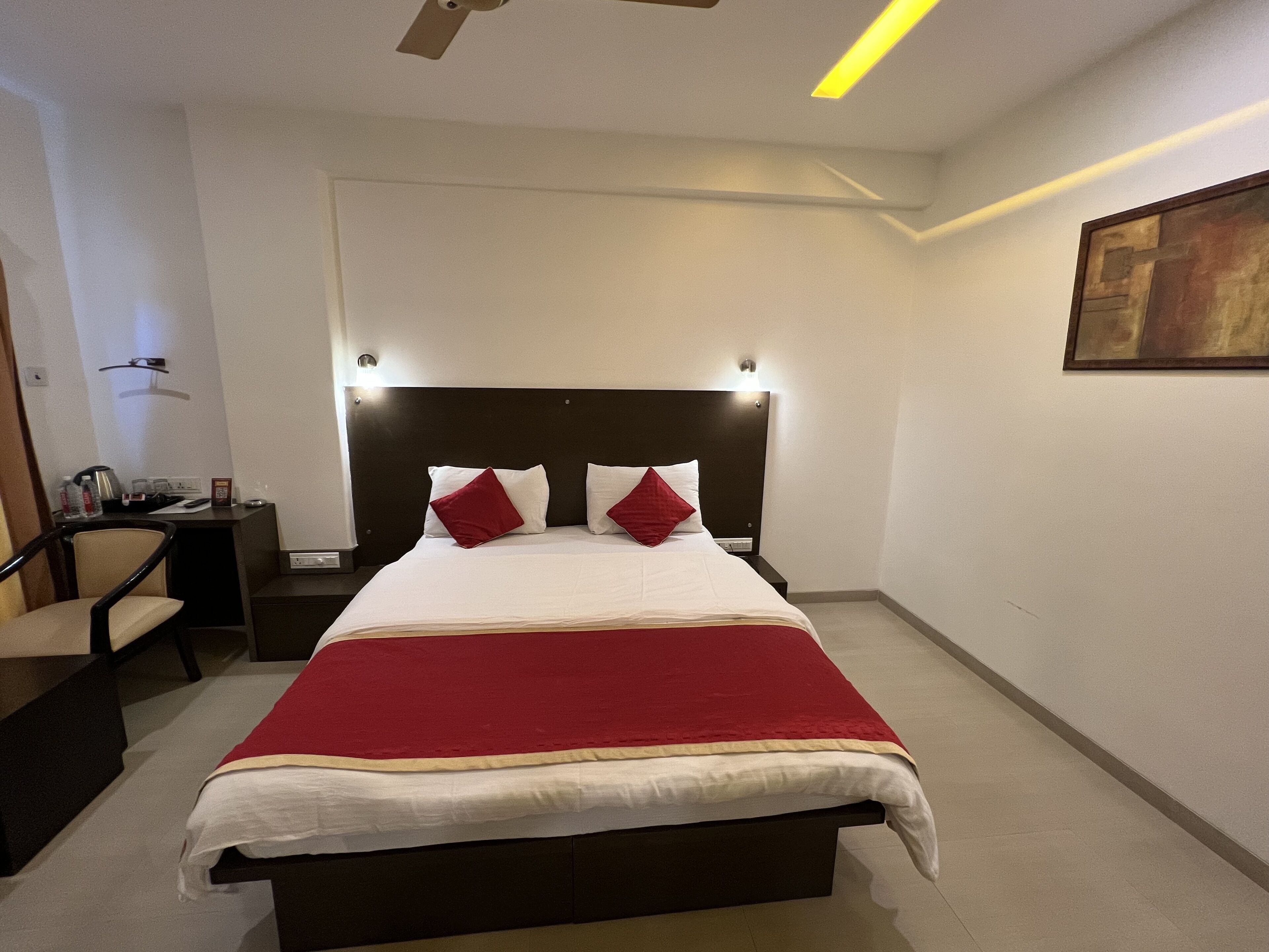 Habitación de hotel ordenada con una cama grande, mesitas de noche, una silla y un cuadro en la pared.