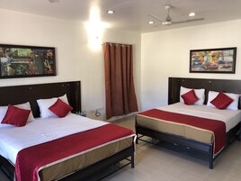 Habitación de hotel con dos camas, cada una con ropa de cama roja y blanca, un ventilador de techo y dos cuadros en las paredes.