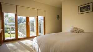 Une chambre avec un grand lit, une porte-fenêtre coulissante donnant sur un balcon et un tableau encadré au mur.