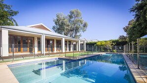 Une piscine à l’eau d’un bleu limpide, entourée d’une clôture et bordée d’un bâtiment doté de grandes fenêtres et d’un patio couvert.