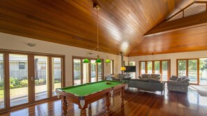 Une pièce spacieuse dotée d’une table de billard, de parquet et de grandes fenêtres offrant une vue sur l’extérieur.