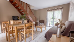 A living room with a wooden dining table, chairs, a sofa, a TV, and a staircase. - Résidence Les Iles (Penestin)