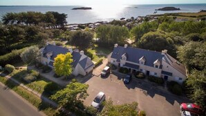 An aerial view of a coastal property with multiple buildings, a parking area, and a clear view of the sea. - Résidence Les Iles (Penestin)