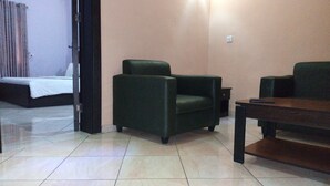 A hotel room with a bed, a green armchair, a wooden table, and a small table lamp. - Eliata Hotel & Suites (Lagos)