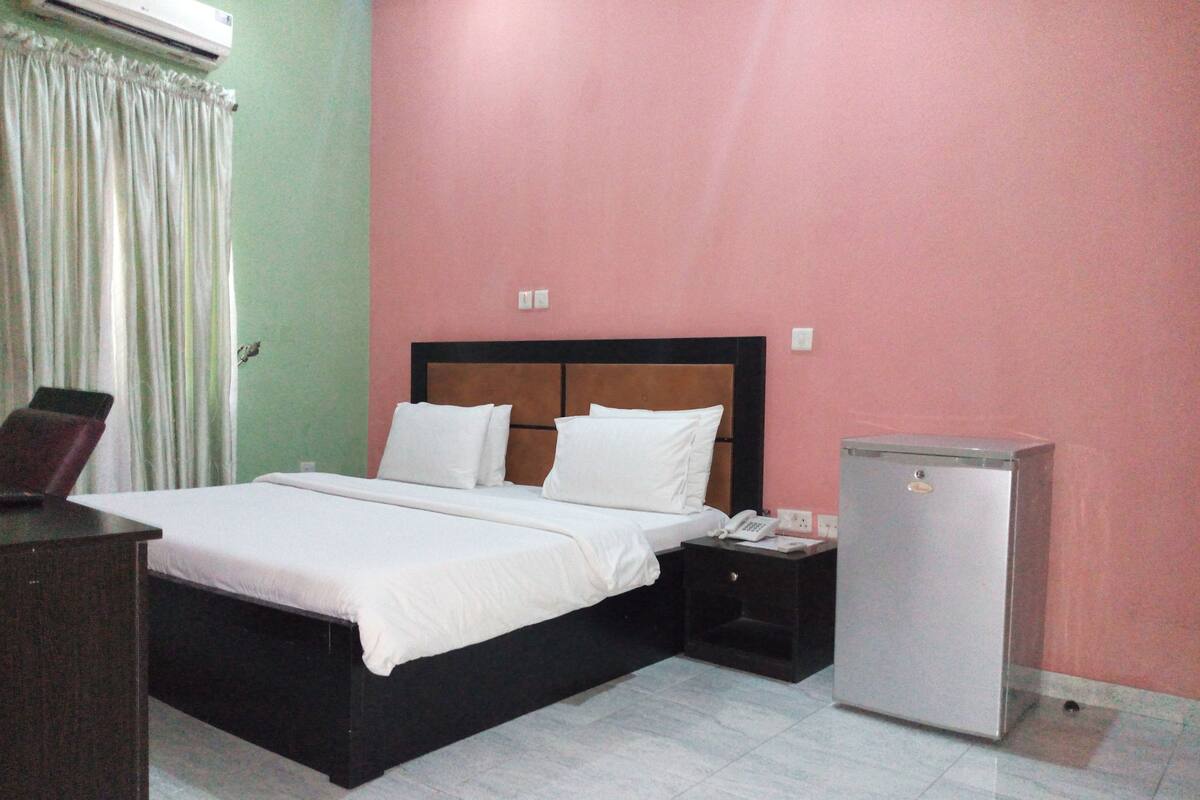 A hotel room with a bed, a nightstand, a desk, and a refrigerator.