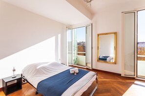 Een slaapkamer met een bed, nachtkastje, spiegel en een schuifdeur die leidt naar een buitenbalkon.