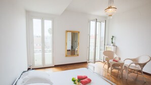 Hotellihuone, jossa on sänky, tuoli, pieni pöytä, peili ja kattokruunu.