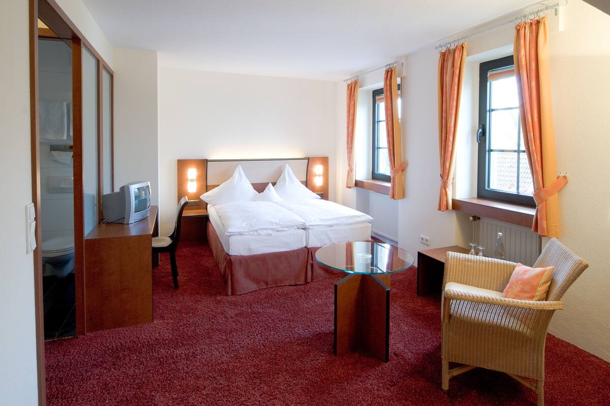 Quarto de hotel com uma cama, uma mesa de vidro, uma cadeira de vime e uma televisão.