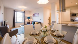 A modern living room with a glass dining table set for four, a sofa, and a kitchen area with a microwave. - King Edward Apartments (Windsor)
