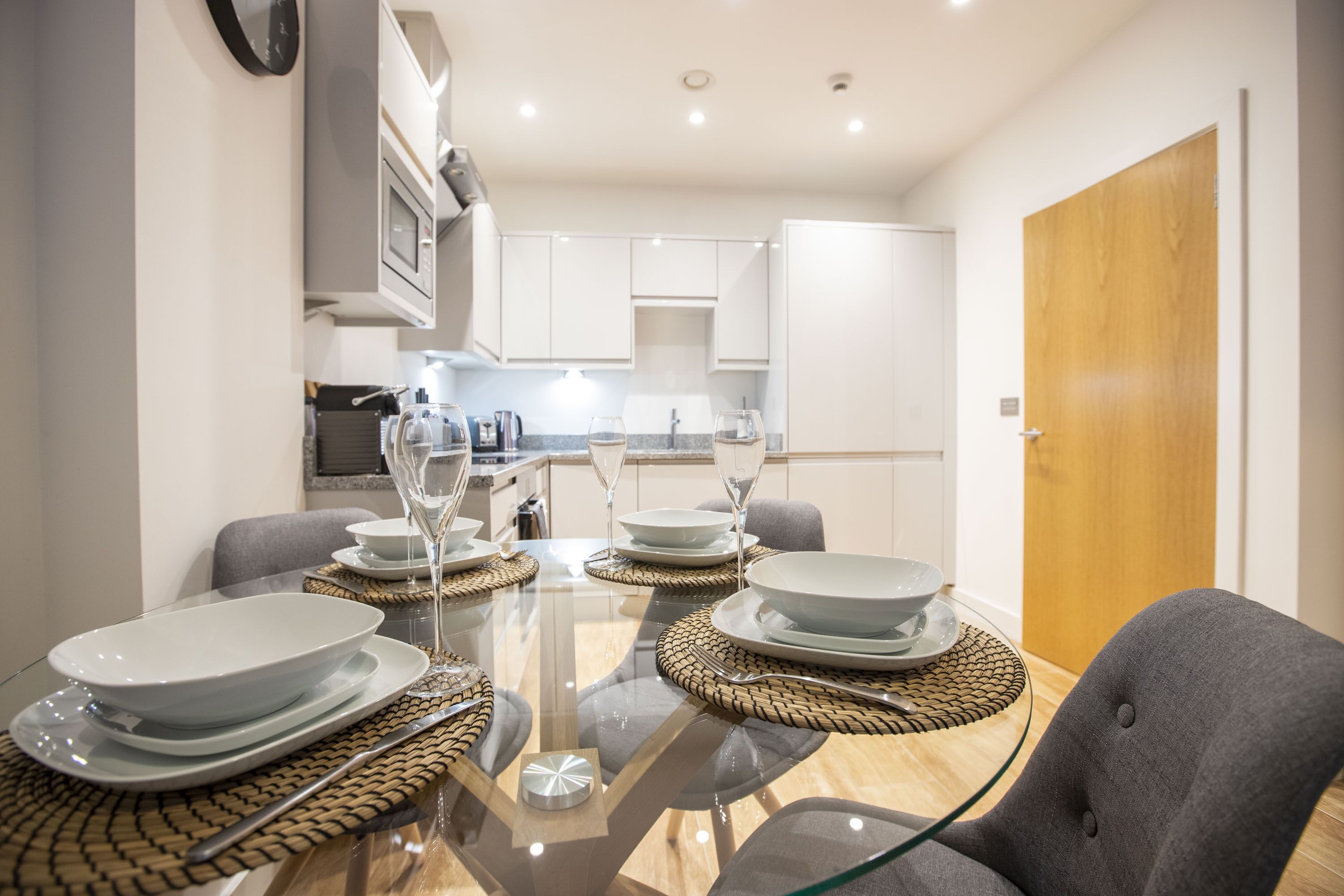 Un espace repas moderne avec une table en verre pour quatre personnes, entourée de chaises grises.