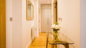 A hallway with a glass table and white flowers, wooden flooring, and a white door. - King Edward Apartments (Windsor)
