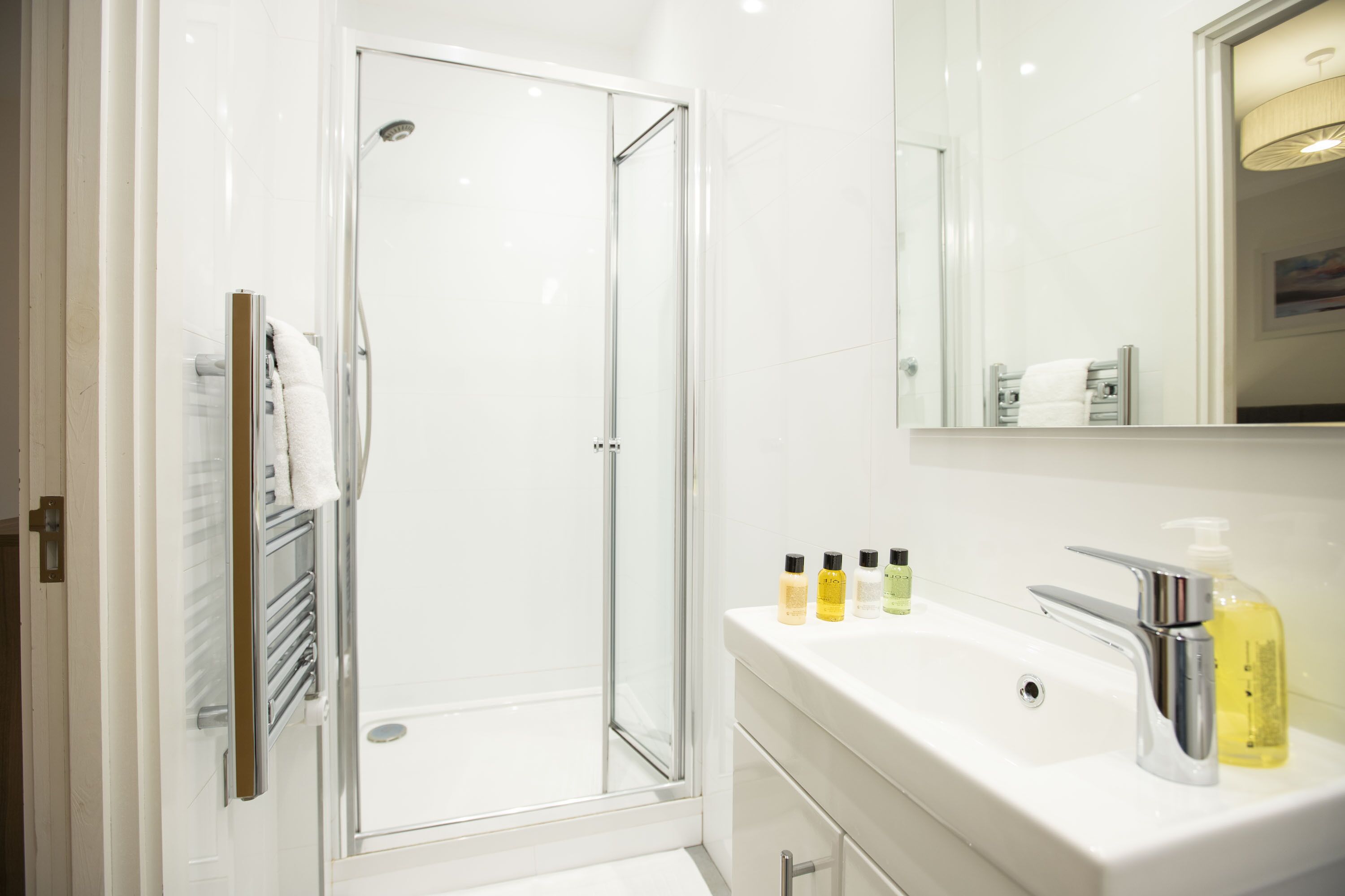 A modern bathroom with a glass-enclosed shower, a white sink with chrome fixtures, and a mirror above the sink.