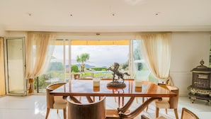 Ein Essbereich mit großem Tisch und Stühlen, einer Statue sowie Blick auf einen Garten und Berge.