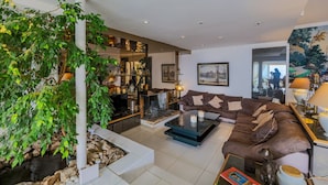 Ein modernes Wohnzimmer mit einem braunen Sofa, einem Glastisch und einer großen Topfpflanze.