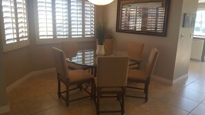 A dining area with a round glass table surrounded by four chairs, a potted plant, and a framed mirror on the wall. - Palm Valley with Beautiful View and Platinum Membership (Palm Desert)