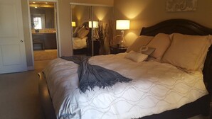 A bedroom with a bed, a nightstand, a mirror, and a door leading to a bathroom. - Palm Valley with Beautiful View and Platinum Membership (Palm Desert)