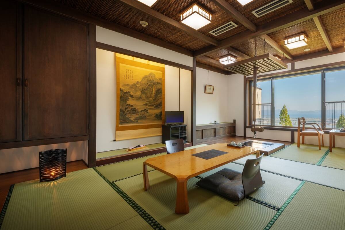 Une pièce de style japonais traditionnel, avec un sol recouvert de tatamis, une table basse, un téléviseur et une grande fenêtre donnant sur un beau paysage.
