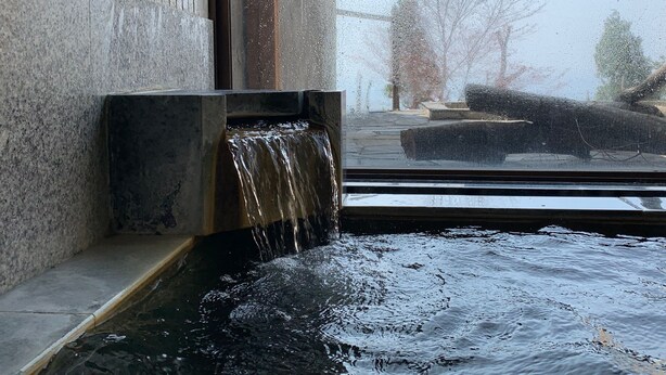 A window with a water feature, a stone wall, and a view of trees and a building outside. - Lake View Inawashirosou (Inawashiro)