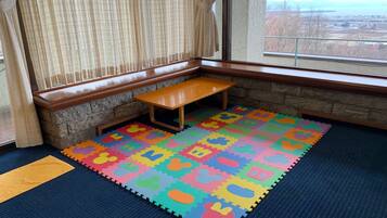 A corner room with a bench, a colorful play mat, and a view of a distant landscape through a window.
