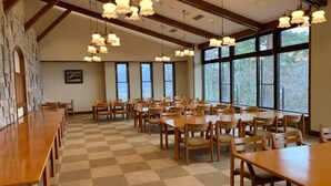 A spacious dining area with wooden tables and chairs, large windows, and hanging pendant lights. - Lake View Inawashirosou (Inawashiro)
