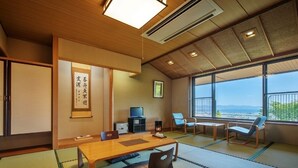 A traditional Japanese room with tatami flooring, a low wooden table, and a view of the sea through large windows. - Lake View Inawashirosou (Inawashiro)