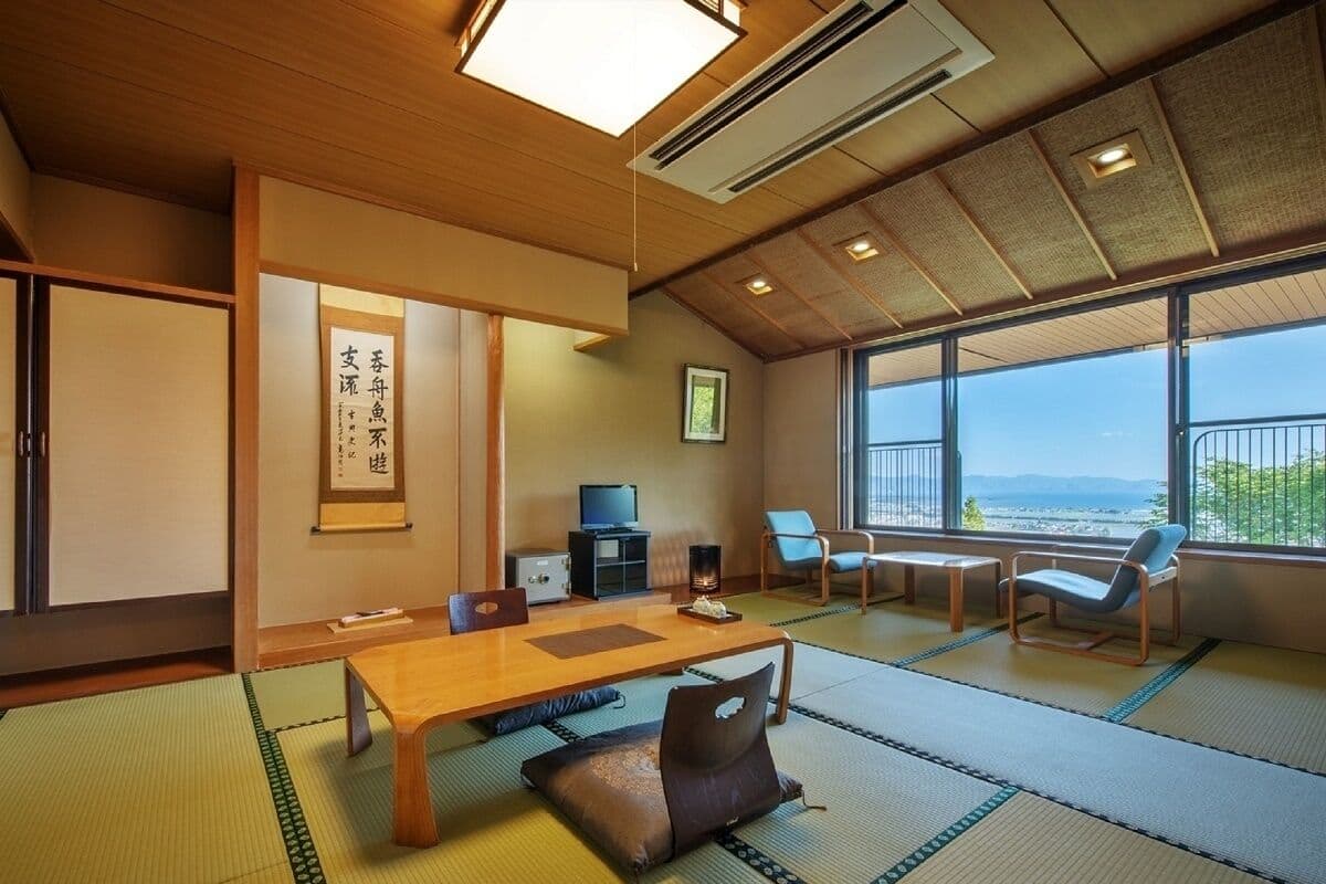 Une pièce de style japonais traditionnel, avec un sol recouvert de tatamis, une petite table en bois et une vue sur la mer grâce à de grandes fenêtres.