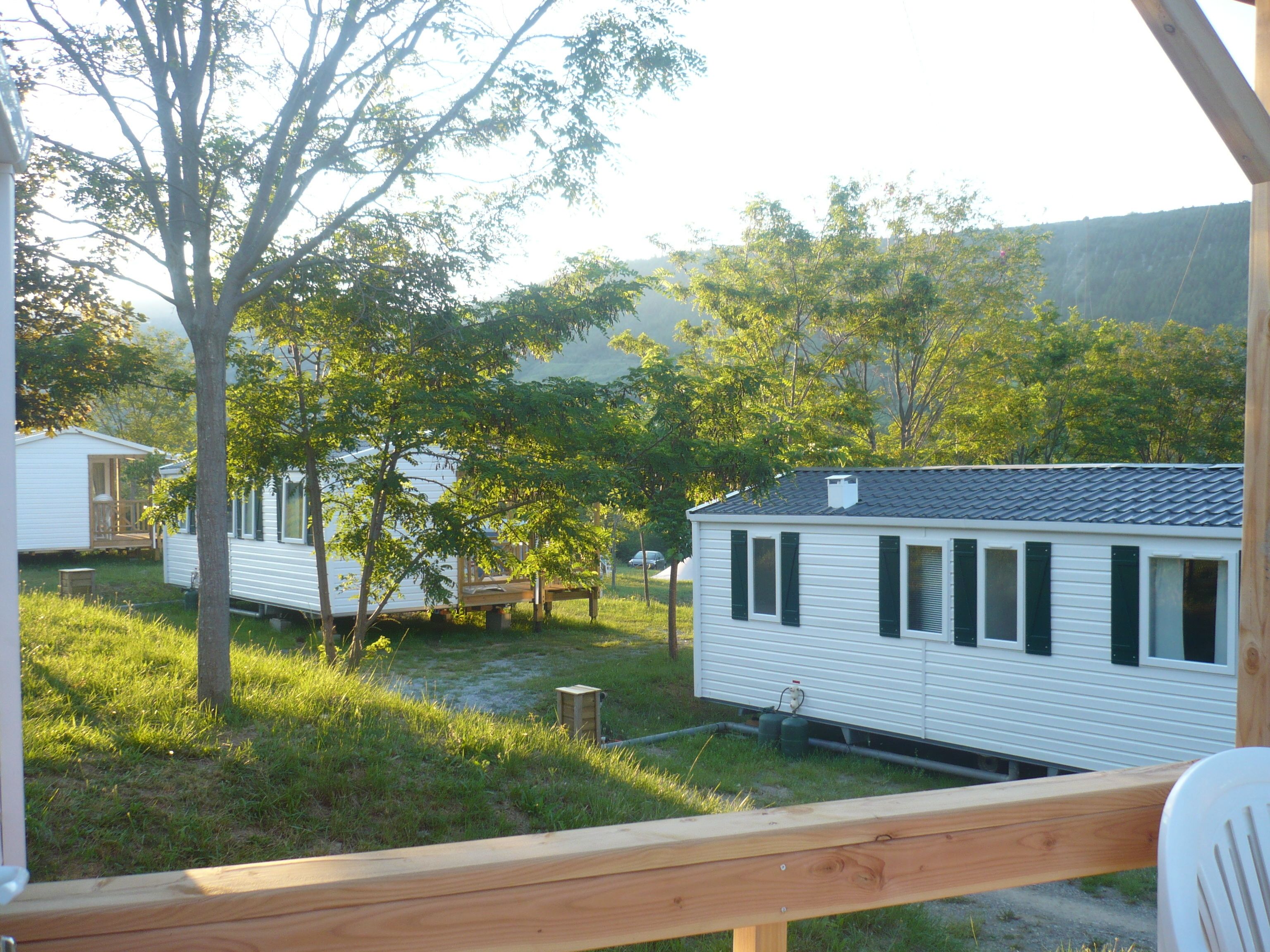 A mobile home with a deck, surrounded by trees and a grassy yard.