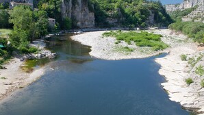 A river with kayaks, rocky banks, and buildings in the background. - Ludocamping Mobil-Home (Lussas)
