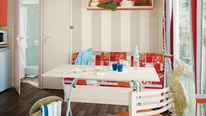 A modern dining area with a white table, striped cushions, and a basket with a towel. - Ludocamping Mobil-Home (Lussas)