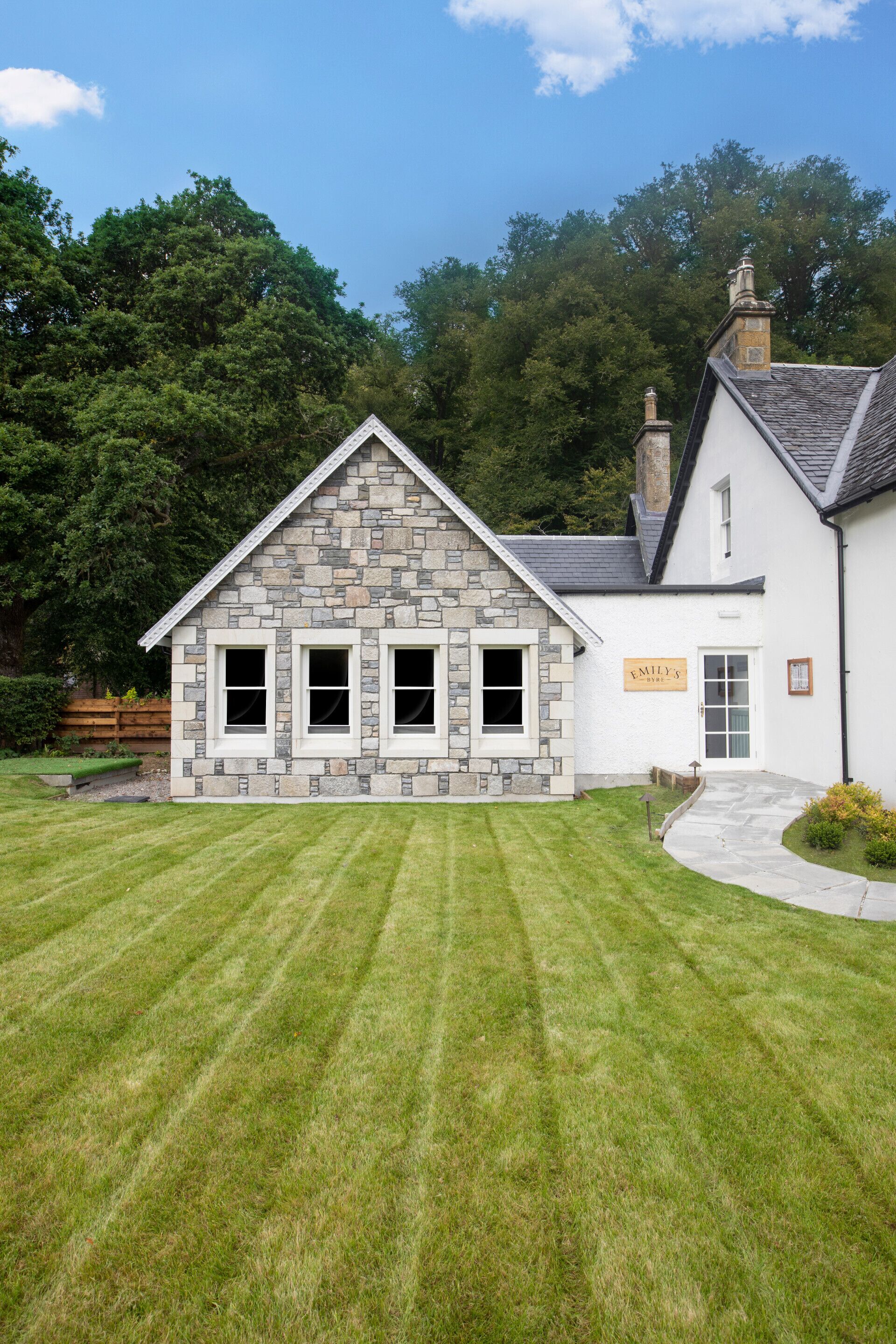 A stone building with a sign reading "EMILY'S" and a well-maintained lawn in front.