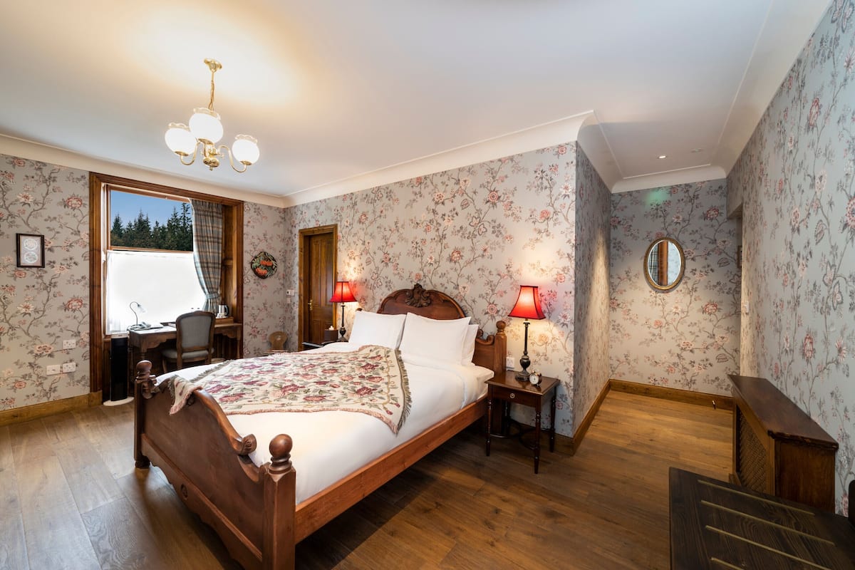 A bedroom with a wooden bed, floral wallpaper, and a desk with a chair.