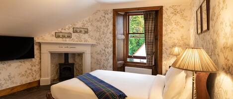 A bedroom with a bed, a fireplace, a window, and a lamp.