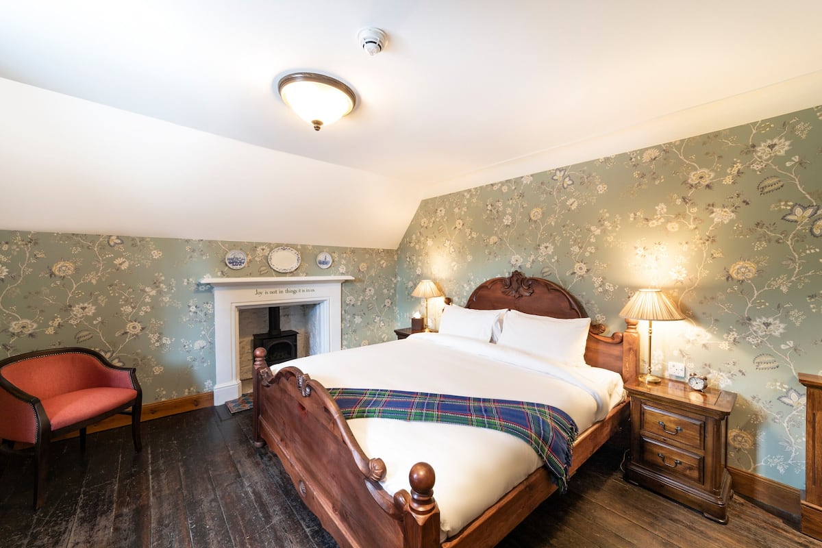 A traditional bedroom with a four-poster bed, a fireplace, and floral wallpaper.