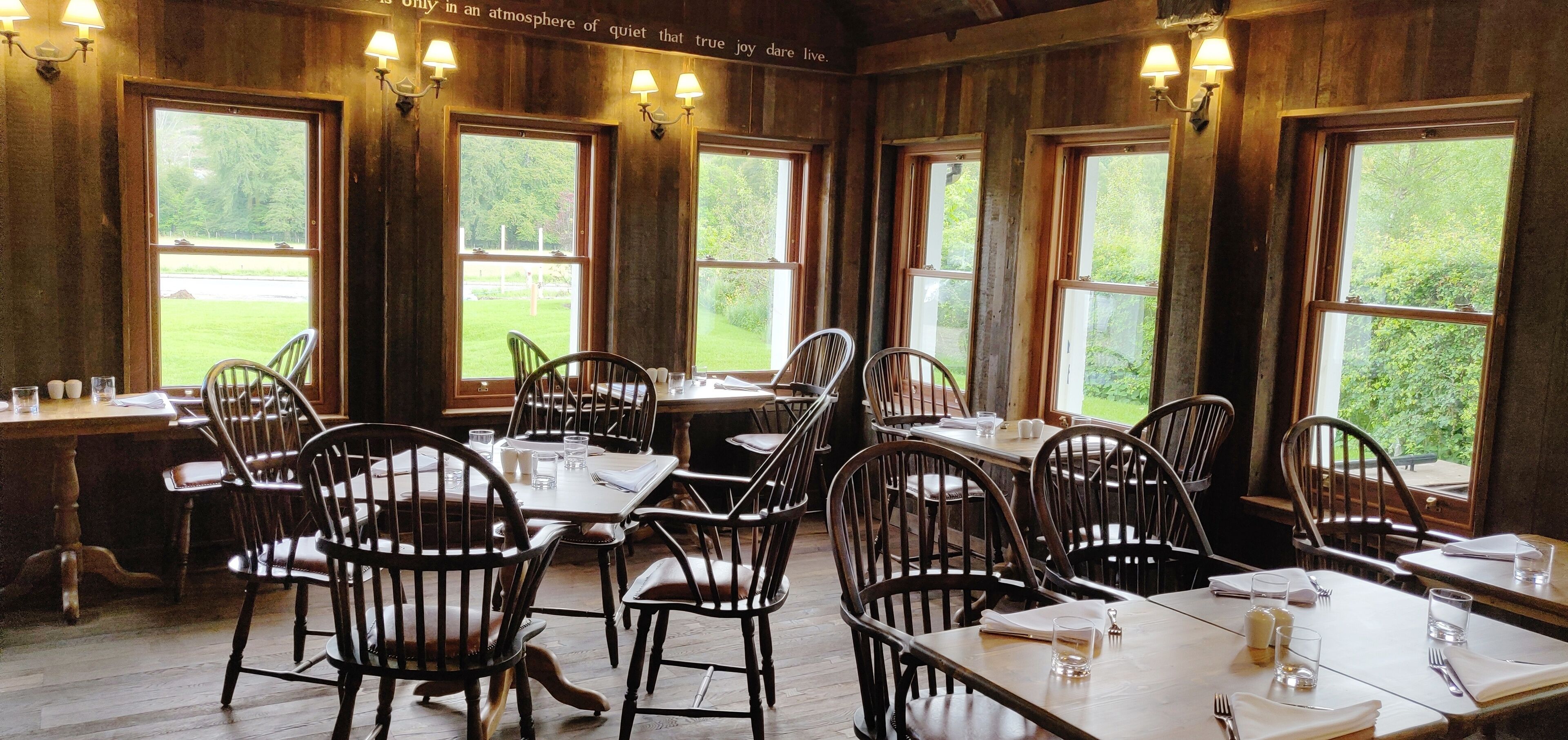 A dining area with wooden walls and large windows, featuring tables and chairs.
