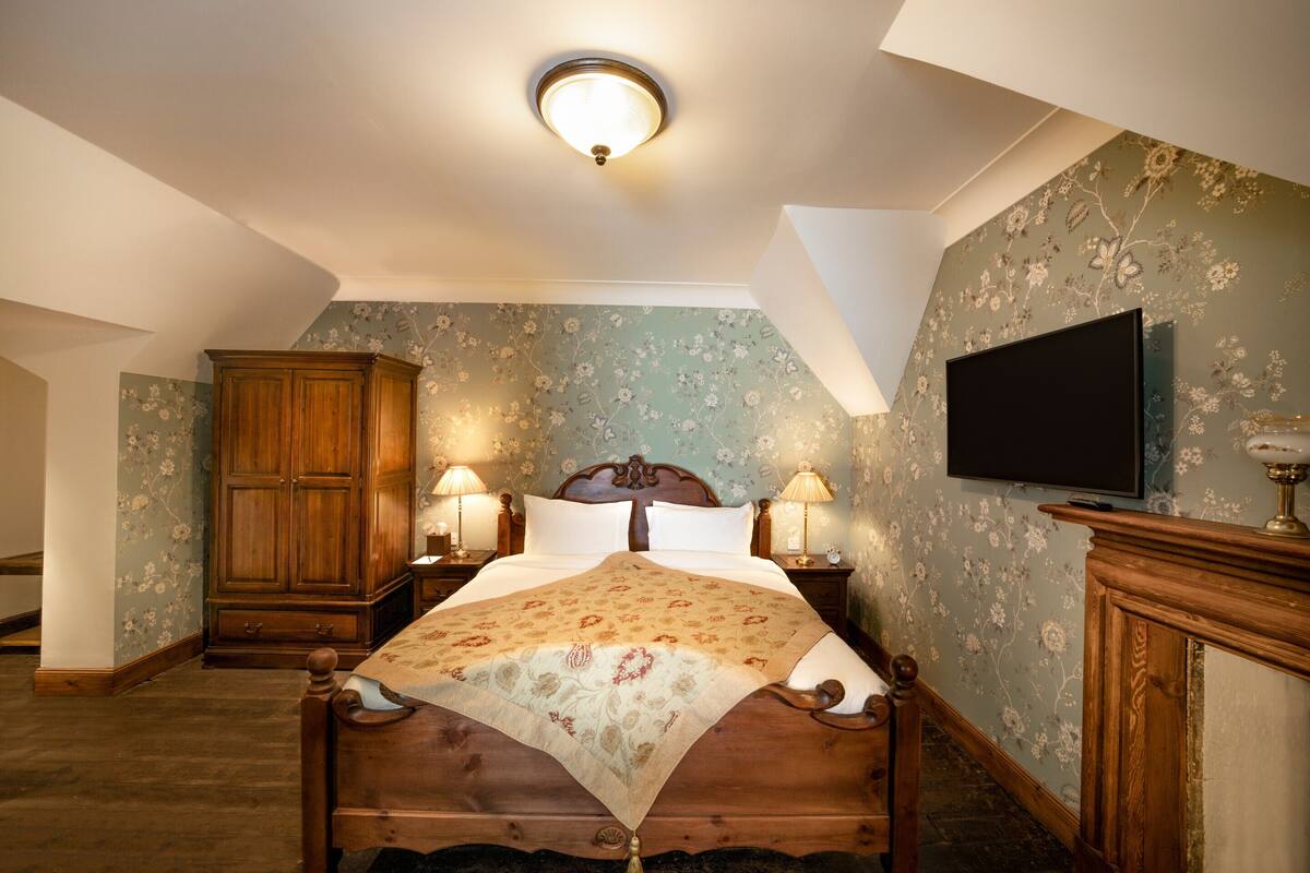 A bedroom with a wooden bed, floral wallpaper, a television, and two bedside lamps.