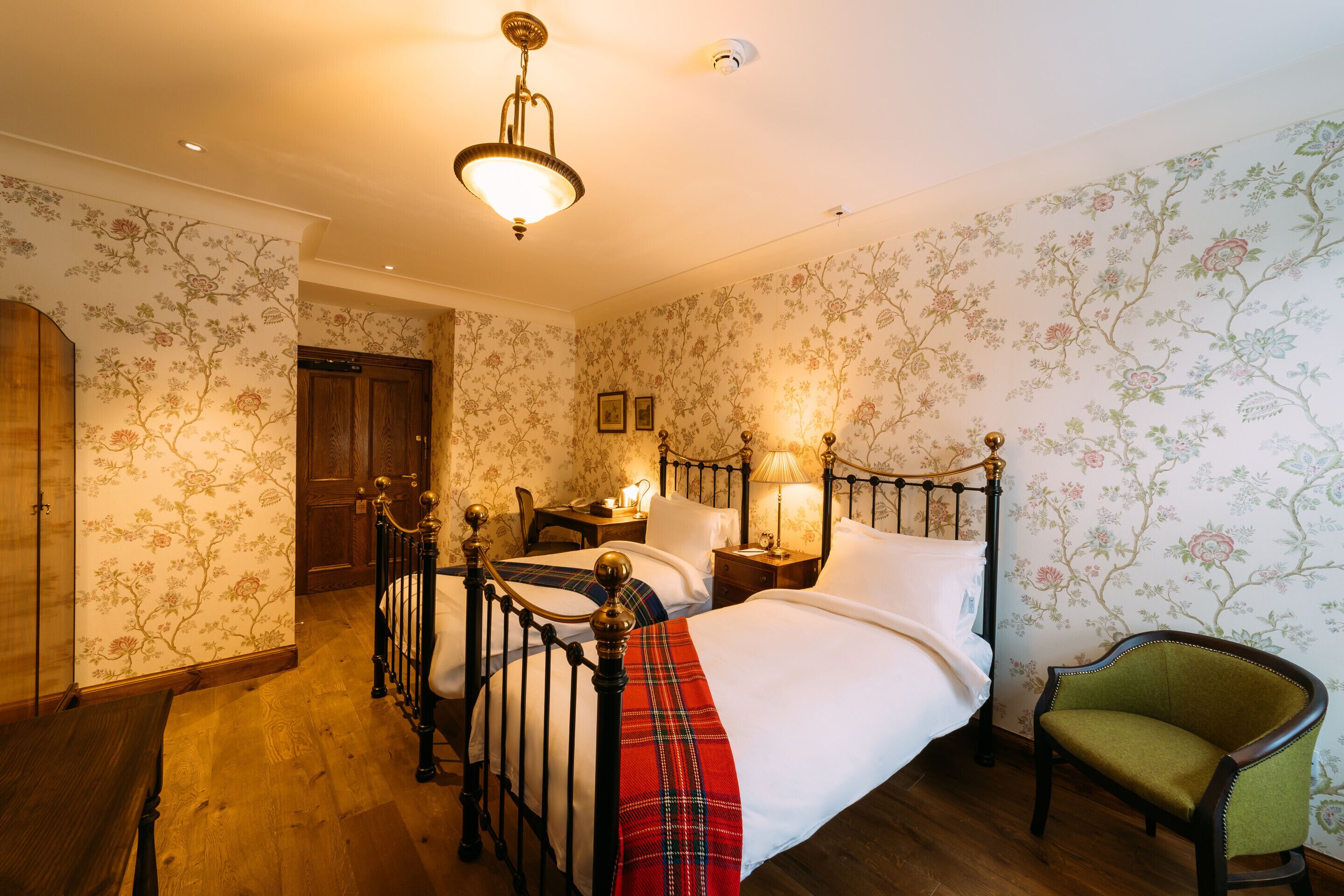 A bedroom with a four-poster bed, a green armchair, and floral wallpaper.