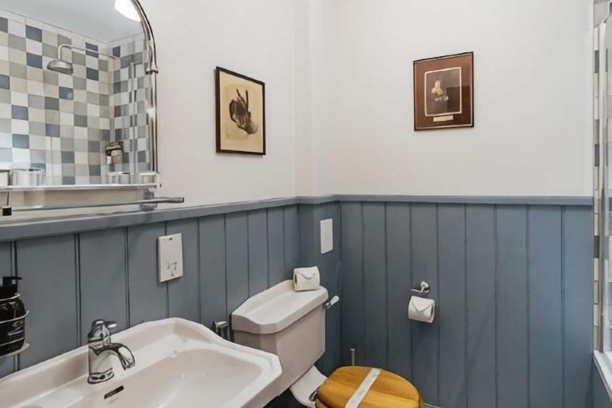 A bathroom with a sink, toilet, mirror, and framed pictures on the wall.