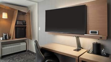 Une chambre d’hôtel équipée d’un téléviseur à écran plat fixé au mur, d’un bureau avec une chaise, d’un four à micro-ondes, d’un mini-réfrigérateur et d’un radiateur.