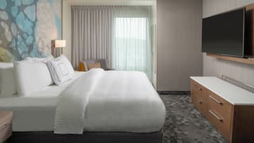 A hotel room with a large bed, a desk, a flat-screen TV, and a window with curtains.