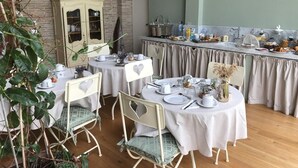 Een eetgedeelte met ronde tafels voor vier personen, witte stoelen en een buffet met verschillende soorten eten.