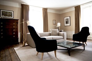 A living room with a sofa, two armchairs, a coffee table, a wooden cabinet, and a floor lamp. - Le 25Bis by Leclerc Briant (Epernay)