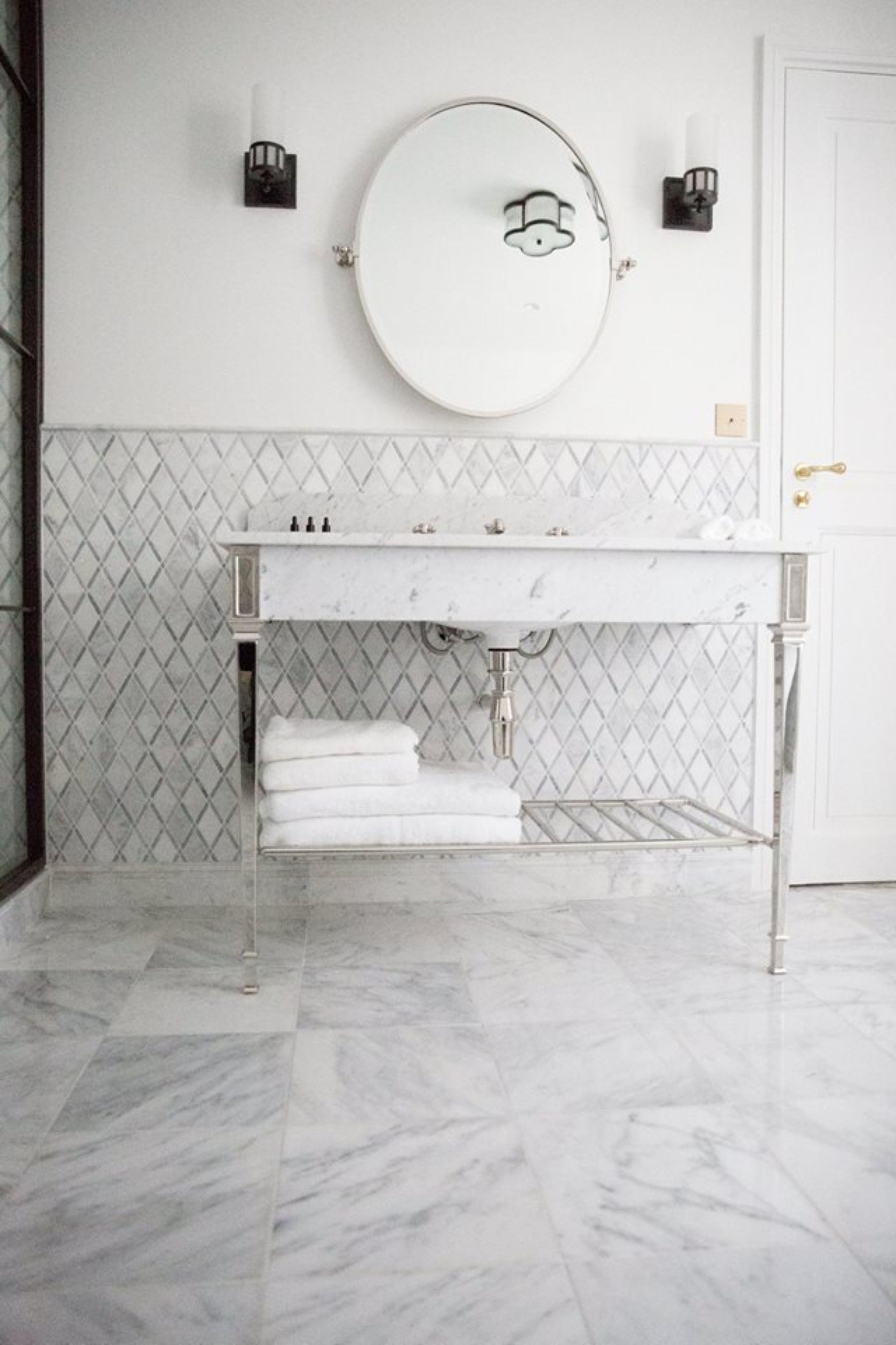 A bathroom with a white marble sink, a round mirror, and a tiled backsplash.